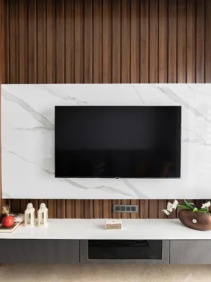 A closer look at the TV unit, which is the focal point of this living room. The combination of white marble laminate, dark wood fluting, and a sleek console creates a sophisticated and contemporary look.