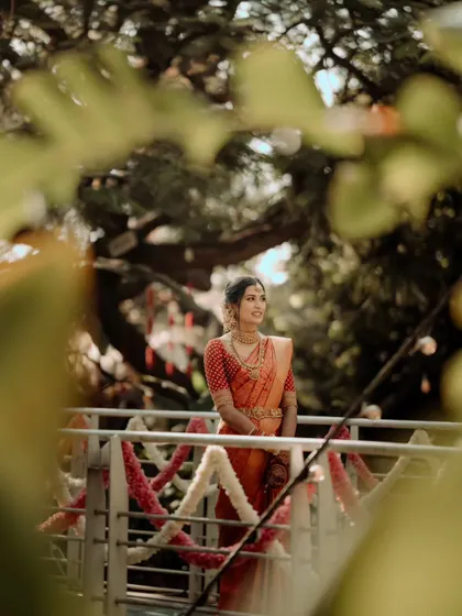 Framed by leaves, the bride stands on a decorated bridge, looking out towards her future. This portrait captures a moment of peaceful anticipation.