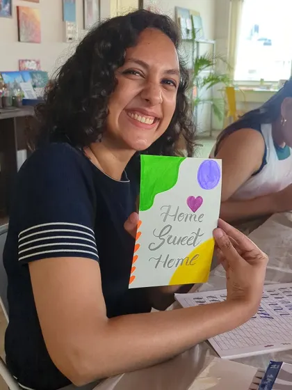 A participant smiling as she shows off her "Home Sweet Home" calligraphy card.