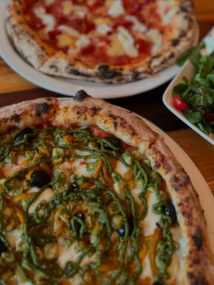A beautiful table spread featuring our Pesto Chicken pizza and a classic Margherita.