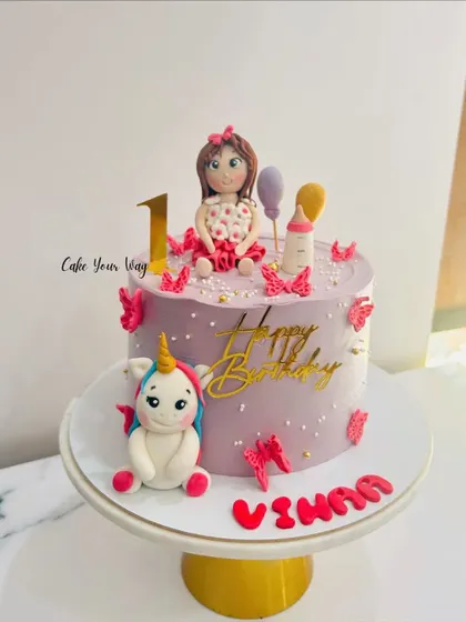 A one-derful first birthday cake with a fondant doll and her unicorn friend, decorated with whimsical butterflies.