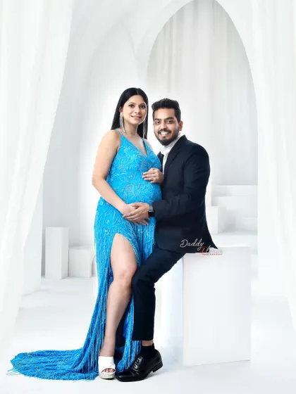 A glamorous couple's portrait in my studio. The expectant mother shines in a sparkling blue sequin gown, showcasing the variety of high-end outfits available in my luxury wardrobe collection.