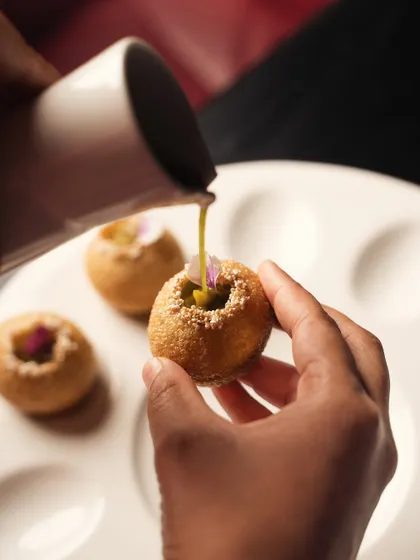 A close-up, interactive shot of spiced water being poured into a pani puri. This action shot makes the experience tangible and is highly engaging for viewers.