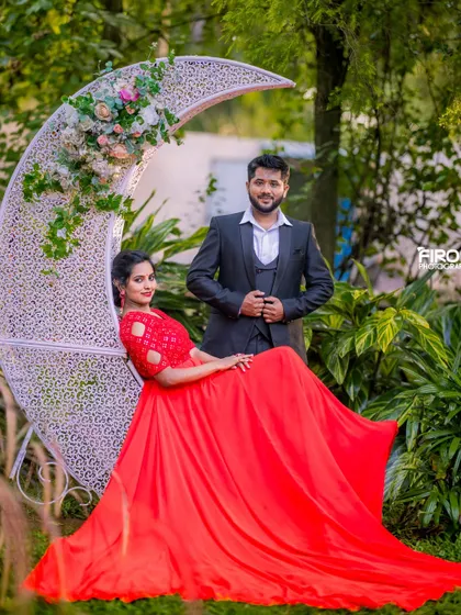 A whimsical and romantic portrait featuring a crescent moon prop. The bride's flowing red dress and the lush garden create a truly magical, fairy-tale scene.