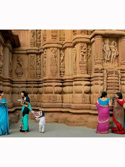 Women in colorful sarees gather outside a temple with intricately carved walls. This image from the Aditya Birla Group series documents a moment of social gathering and celebration within a sacred space.