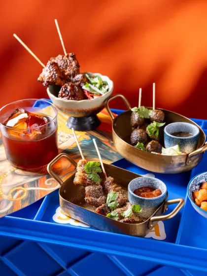 A vibrant shot of appetizers and a drink at Banng Bar. The contrast between the bright blue tray and the warm orange background makes the colors pop, creating a visually exciting composition.