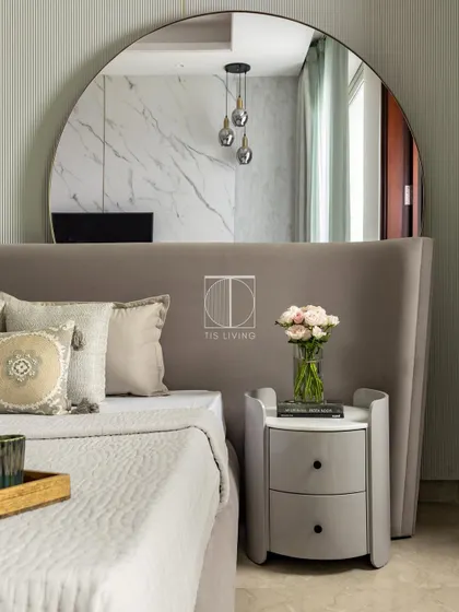A detail of the guest bedroom, showing the elegant curve of the wingback headboard and the custom-designed rounded nightstand. The large mirror reflects the light and makes the space feel larger.