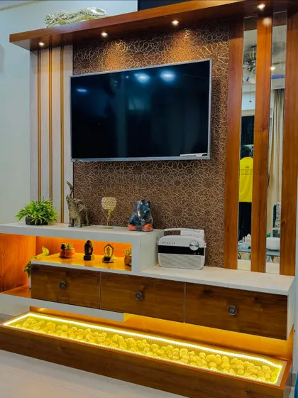 This TV unit design is all about luxury and function. It features a textured back panel, a white marble-finish console with open and closed storage, and a unique illuminated pebble tray at the bottom.
