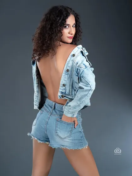 This backless denim-on-denim look is captured in the studio against a simple grey backdrop. The focus is on the casual yet confident pose and the texture of the fabric, creating a classic and timeless fashion portrait.