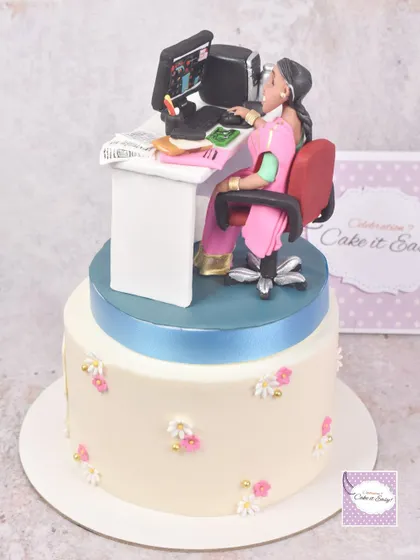 This two-tier cake for a 60th birthday features a detailed keepsake topper of the recipient at her work desk, celebrating her career as a PCB engineer.