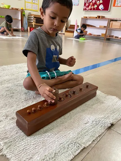The Cylinder Blocks are a foundational sensorial material. By fitting each cylinder into its correct socket, the child refines their pincer grip for writing and develops their ability to visually discriminate between different dimensions.