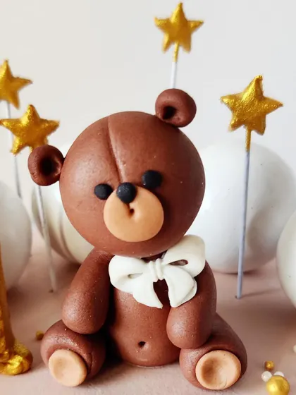 A detailed shot of the hand-sculpted fondant teddy bear with a white bow. This little guy is ready to celebrate a special first birthday.