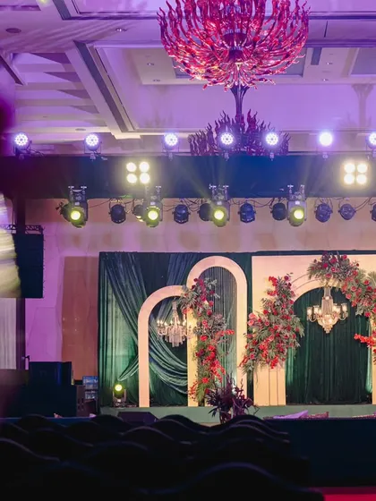 The stage for this modern Sangeet featured a backdrop of emerald green velvet and elegant gilded arches, asymmetrically decorated with crimson floral arrangements for a contemporary, artistic feel.
