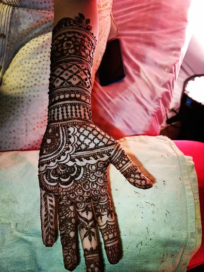 A detailed party mehendi design that extends up the forearm. The combination of curved paisleys on the palm and structured bands on the arm creates a balanced composition.