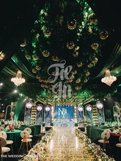 This is our 'Savannah Splendour' Sangeet, where we transformed a ballroom into a tropical wonderland. The design features a lush green ceiling with a cascade of gold mirror balls, a custom glass aisle filled with fairy lights, and opulent seating in jewel tones, demonstrating our capability for large-scale, thematic event production.