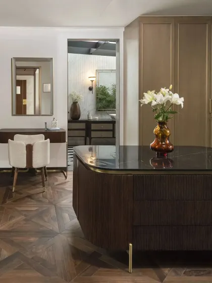 A walk-in closet and dressing area featuring a central island with a dark stone top and ribbed wood detailing. The design combines engineered wood flooring with custom cabinetry for a highly functional and luxurious space.
