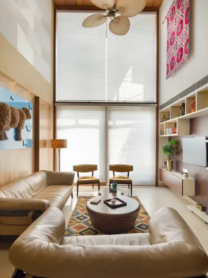 The double-height living room in Kavyam Residence is flooded with natural light. Custom-designed furniture, including curved leather sofas, creates a warm setting, while curated wallpapers and murals add texture and personality.
