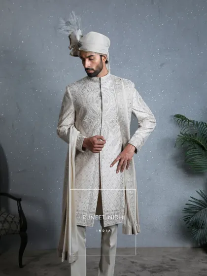 Crafted in a luxurious ivory silk base, this sherwani is adorned with intricate resham embroidery. Elaborate paisley and floral patterns grace the chest and shoulders, creating an heirloom of elegance.