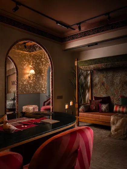 A moody, atmospheric shot of the client interaction zone. The custom daybed, upholstered in a rich botanical print, sits opposite the curved desk, creating a luxurious yet comfortable space for conversation and collaboration.