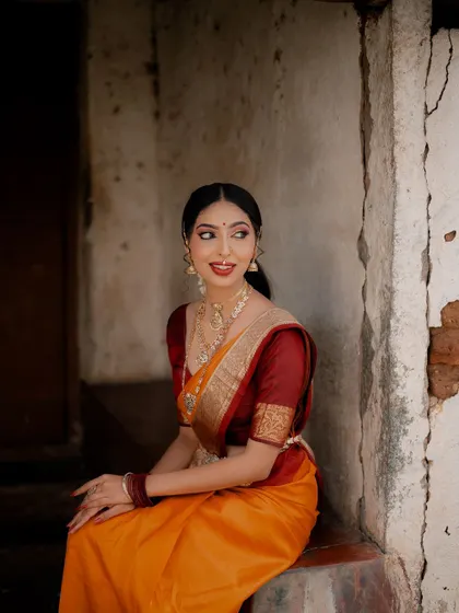 A candid, seated portrait. The bride's relaxed pose and the rustic setting create a beautiful contrast, making the elegance of her saree and jewelry stand out.