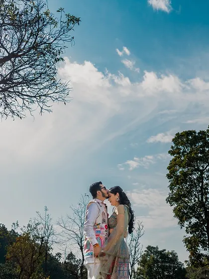A low-angle shot of the couple against a vast blue sky, making their love feel as grand as the world around them.