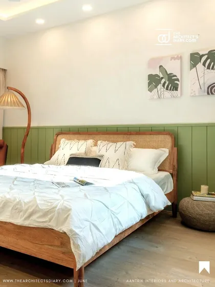 A bedroom from the 'Tranquil Tones' project, featured in The Architect's Diary. The design pairs a cane and wood bed frame with a soothing green accent wall and botanical art.