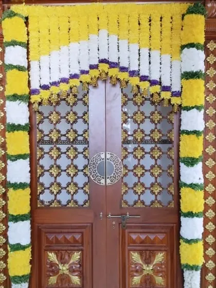 A pooja room door decorated with yellow and white flower garlands. This design complements the traditional aesthetic of the ornate wooden door.