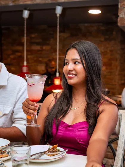 A guest smiles, holding a beautiful pink cocktail. Our "Pastas from Ancient Rome" event was a celebration of food, history, and good company, where every moment was a delight.