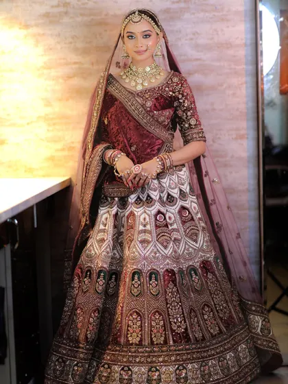 A full view of the bride, standing gracefully. The Polki jewellery set adds a brilliant sparkle that contrasts beautifully with the rich, dark fabric of her outfit.
