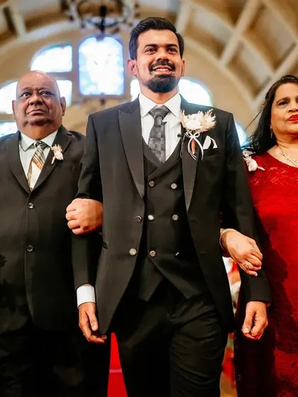 The groom makes his grand entrance, proudly escorted down the aisle by his parents.