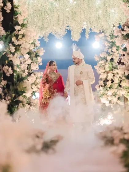 A magical wedding portrait of the couple standing under a floral arch, surrounded by ethereal smoke.