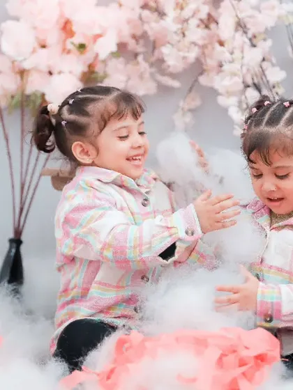 Twin sisters playing with soft, cloud-like props in our studio, surrounded by pink floral decorations.