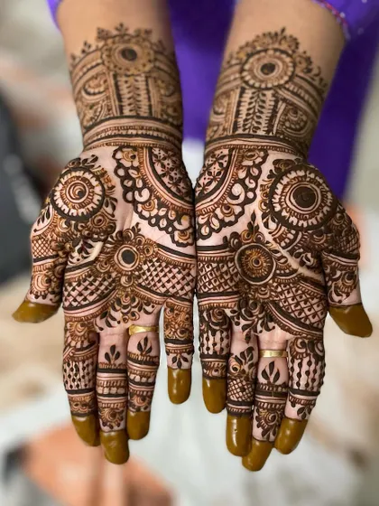 A bold, symmetrical design featuring prominent circular elements and detailed checkerboard filling. The solid henna on the fingertips provides a beautiful contrast.