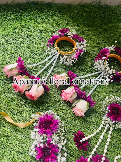 A Haldi jewellery set for a bride and her bridesmaids. This set features haath phool and kaliree made with pink roses, purple chrysanthemums, and baby's breath.