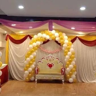 A classic stage decoration for a baby shower or naming ceremony, with a yellow and white balloon arch and a special chair.