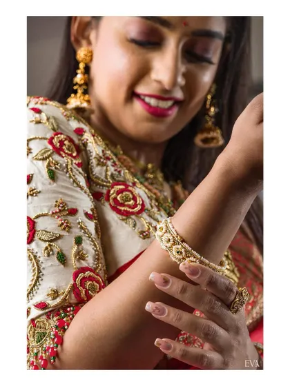 A close-up shot focusing on the detailed floral embroidery of the blouse and the delicate design of the gold bangle. This highlights the craftsmanship of both the apparel and accessories.