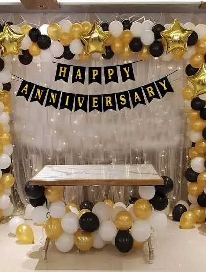 A classic anniversary decoration with a black, gold, and white balloon arch and a 'Happy Anniversary' banner.