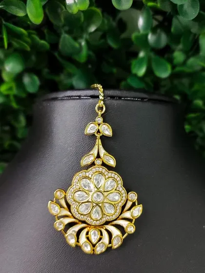 A delicate and elegant maang tikka with a floral design made of kundan stones. The white enamel detailing adds a modern and sophisticated touch.