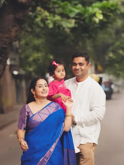 A classic family walking portrait. This outdoor shot captures the family in a natural, candid moment, beautifully framed by the soft light and greenery.