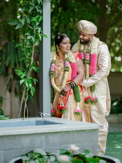 A classic portrait of the bride and groom by a water feature, their garlands adding a beautiful touch of tradition.