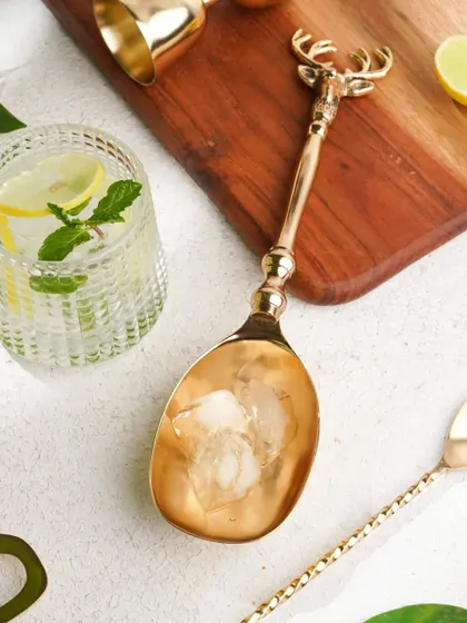 A close-up of a golden, deer-themed ice scoop, highlighting the intricate design and luxurious feel of the barware.