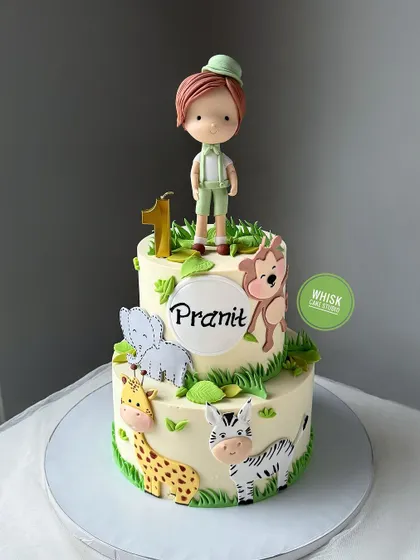 A sweet jungle safari cake for a first birthday. This two-tiered cake features 2D and 3D handcrafted animals and a cute boy figurine on top.