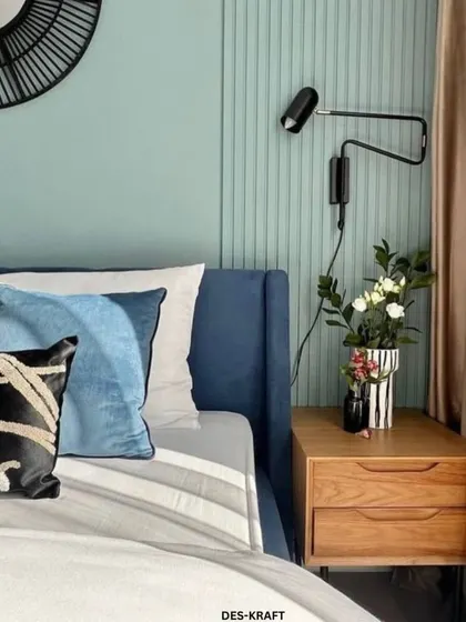 A close-up of the bedside table, where a modern swing-arm sconce provides focused light for reading, complementing the room's tranquil color scheme.