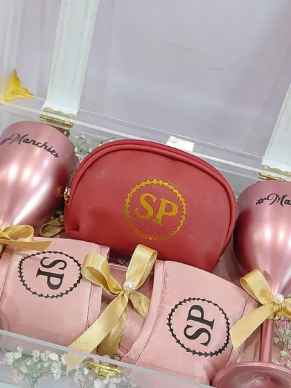 An elegant bridesmaid hamper in an acrylic box, featuring personalized rose-gold wine glasses and other custom items.