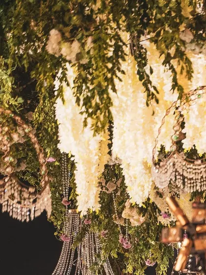 Detail is everything. This shot captures the intricate beauty of a ceiling installation, where cascading white wisteria, crystal elements, and vintage-style bulbs come together to form a canopy of light and flowers.