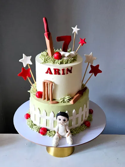 Another take on the cricket theme, this two-tiered cake is perfect for a 7th birthday. It includes a cute cricketer figurine, edible wickets, a bat, and ball, all set on a green pitch.