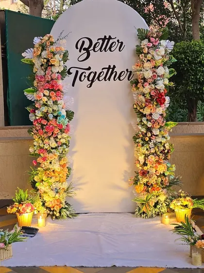 A beautiful and lush floral backdrop for a romantic celebration. I used two large pillars of fresh, multi-colored flowers to frame a simple white panel with the message "Better Together," creating a perfect photo spot for the couple.