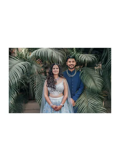 A lovely portrait of the engaged couple against a backdrop of lush palm leaves. Their coordinated blue outfits and happy smiles make for a stunning picture.