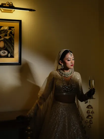 An elegant portrait of the bride holding a glass of champagne, looking down at her kaleeras. A moment of quiet reflection before the ceremony.