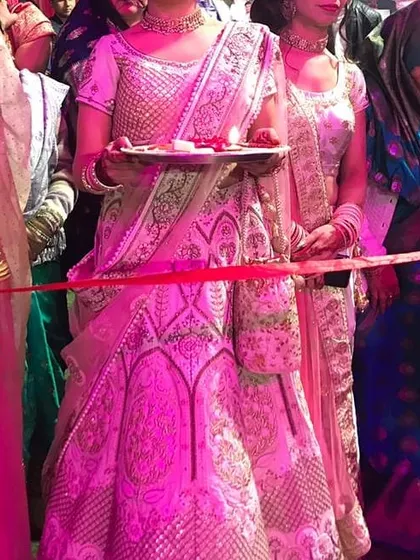 Our client participating in a wedding ritual while wearing the rented ivory lehenga. The outfit looks stunning even under the vibrant pink lighting of the event.